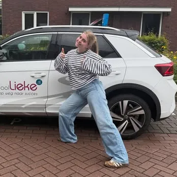 Leerling poseert met duim omhoog bij de lesauto